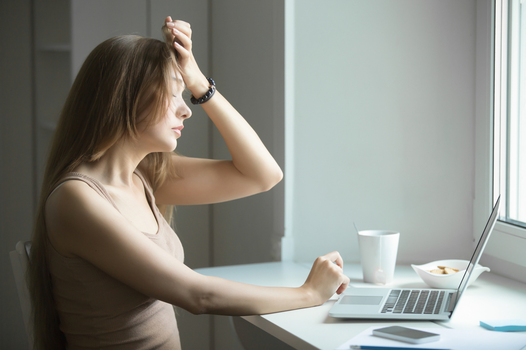 mulher na frente de notebook com mão na cabeça expressando dor de cefaleia